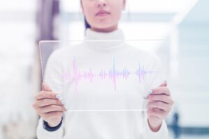 Person holding a transparent digital tablet displaying colorful sound wave graphics, symbolizing voice recognition technology. Image by Freepik.