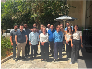 A group photo of the ALFIE project consortium members standing together outdoors in a sunny courtyard during a general assembly meeting