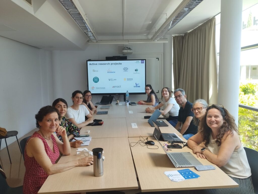 Representatives from the ALFIE project and Transmedia Catalonia team meeting with researchers at the Computer Vision Centre (CVC), seated at a long conference table with laptops open, facing a screen showcasing active research initiatives.