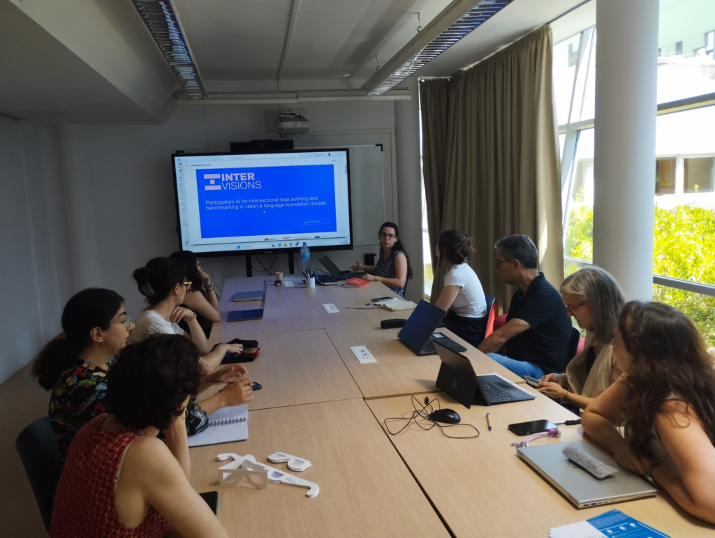 A research presentation during the ALFIE project's visit to the Computer Vision Centre (CVC), showing a presenter discussing the InterVisions project slide on participatory AI and bias auditing to attendees seated with laptops at a conference table.