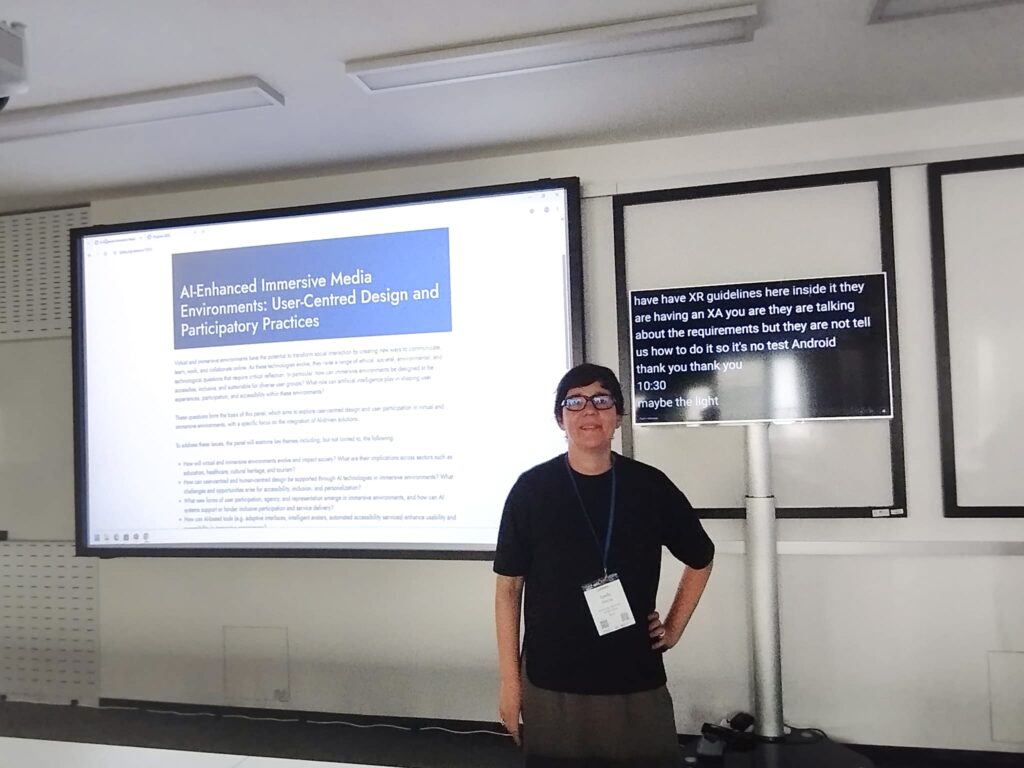 Estel·la Oncins standing at a conference presentation. The screen behind her highlights a panel on AI-enhanced immersive media, user-centred design, and accessibility, alongside a live captioning monitor
